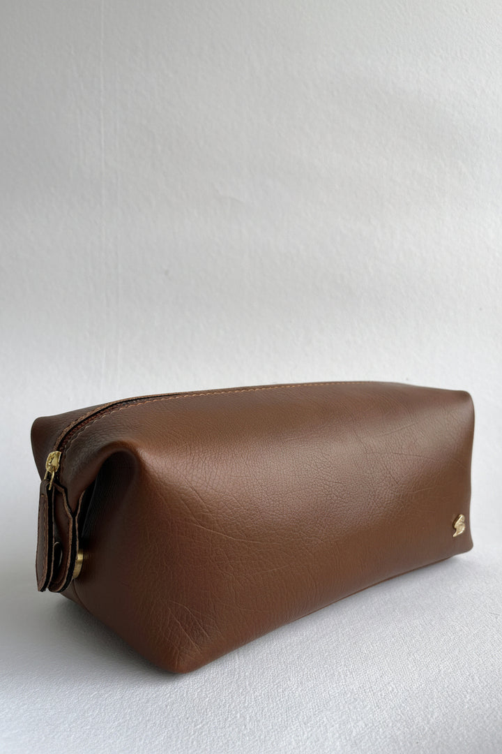 Brown leather toiletry bag with gold zipper on a white background